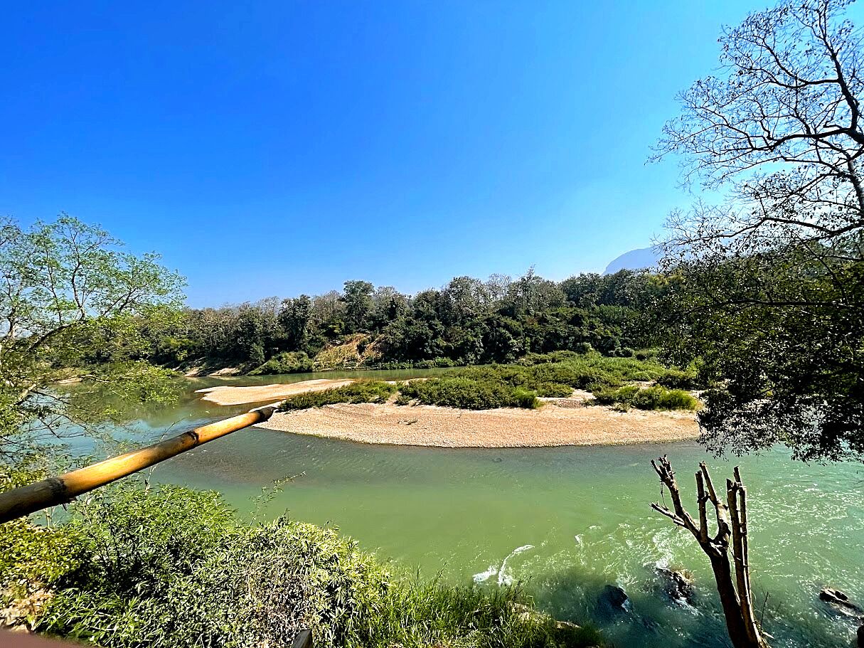 Un río con un puente de madera, rodeado de abundante vegetación y árboles.