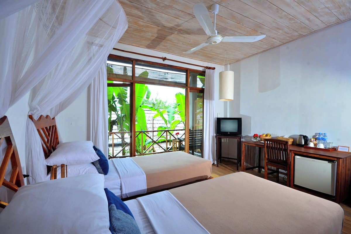 Une chambre d’hôtel avec deux lits, une télévision, un bureau avec un ordinateur et un balcon donnant sur un espace verdoyant.