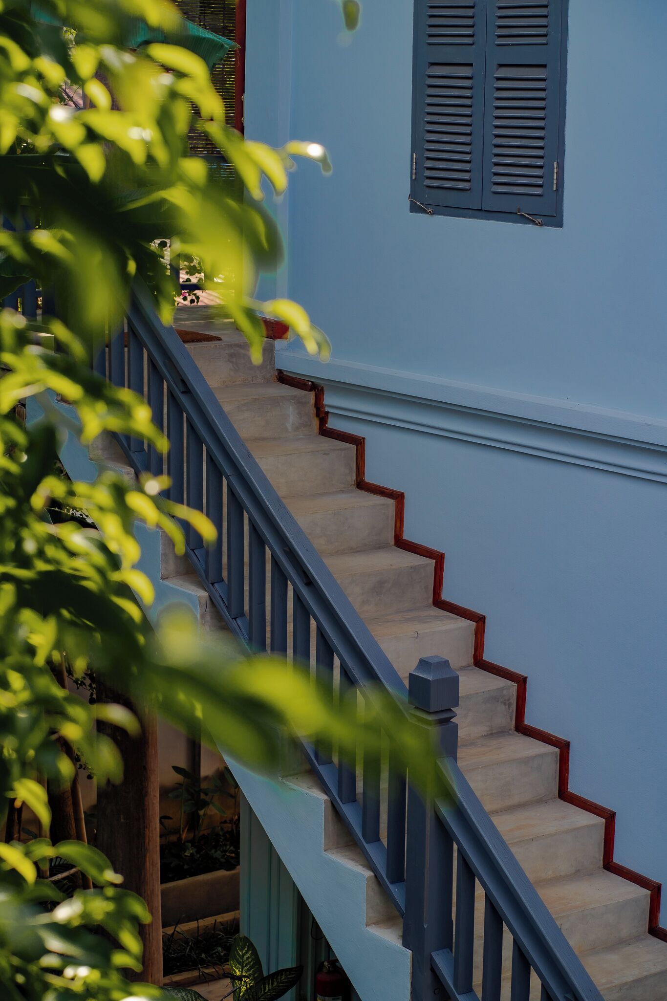A staircase with a blue railing and red trim, leading to a window with shutters.