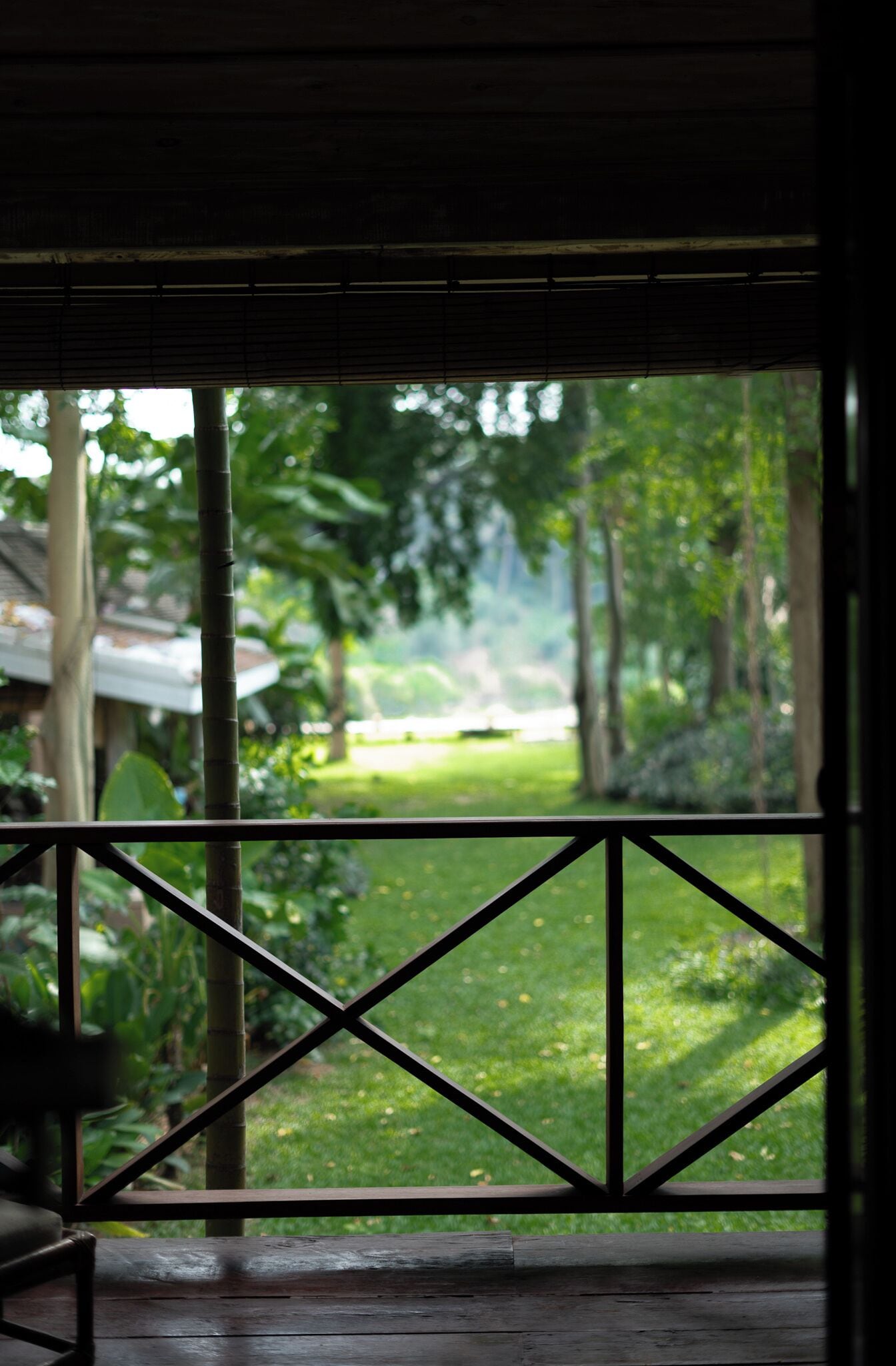 A wooden deck with a metal railing, overlooking a lush green garden with trees and a lawn.