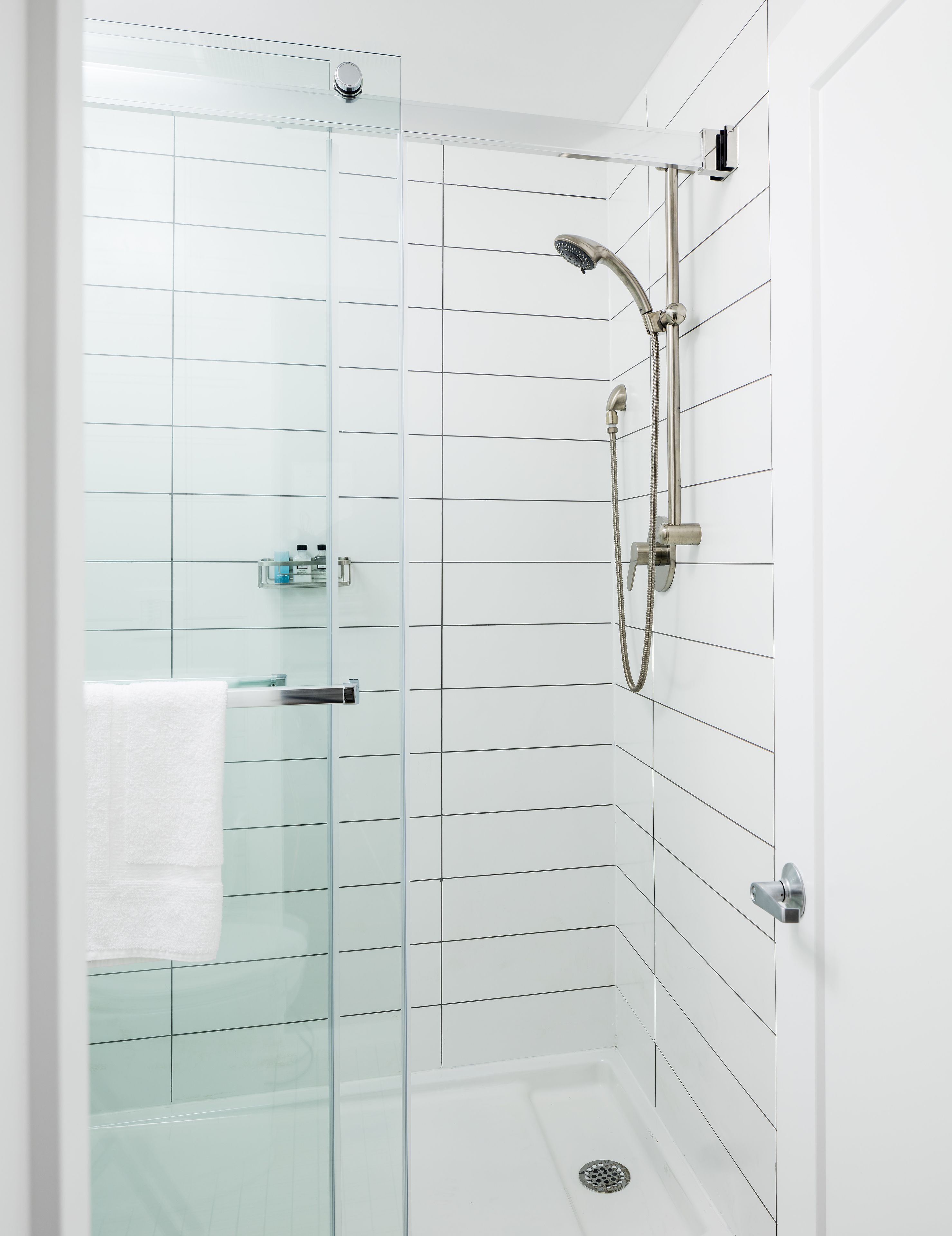 A modern shower with a glass door, a handheld showerhead, and a wall-mounted faucet.