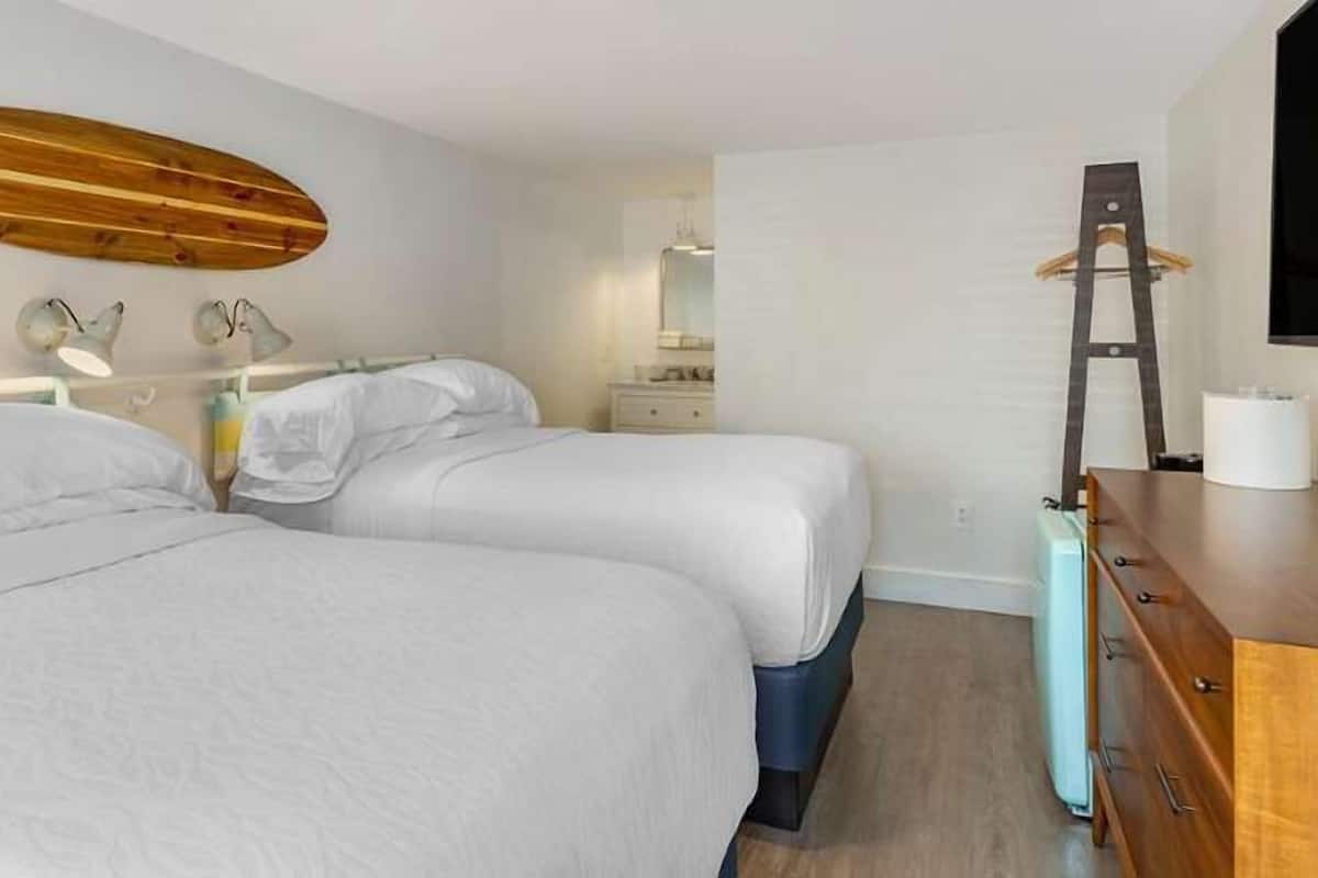 A hotel room with two beds, a wooden surfboard on the wall, a dresser, and a television.
