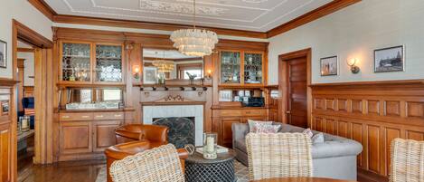 A spacious living room with a wooden floor, a fireplace, and a large chandelier.