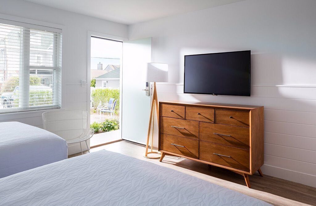A modern bedroom with a large bed, a wooden dresser, a television, and a view of the outdoors.