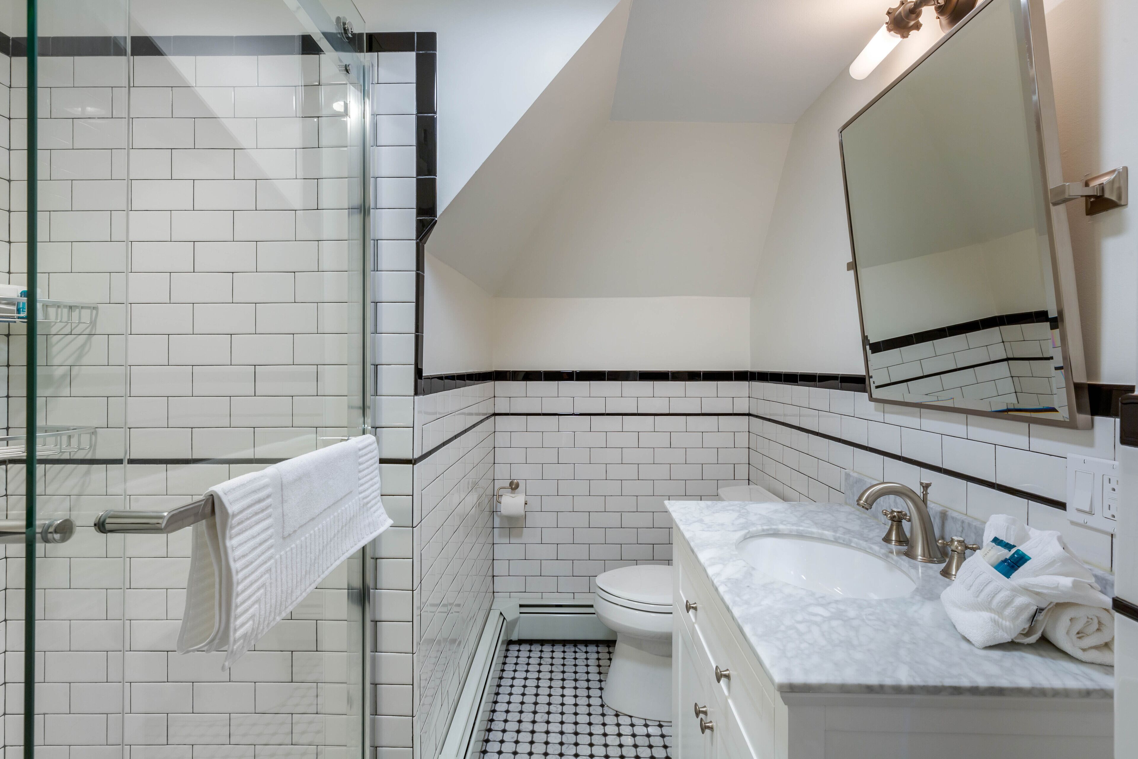 Un baño moderno con cabina de ducha de vidrio, inodoro blanco y lavabo de mármol con espejo superior.