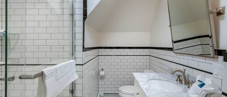 Un baño moderno con cabina de ducha de vidrio, inodoro blanco y lavabo de mármol con espejo superior.