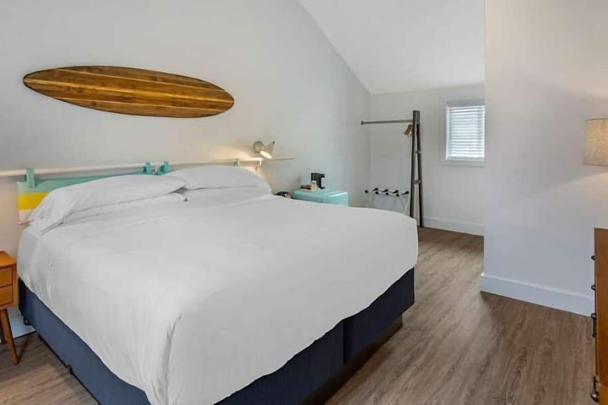A bedroom with a bed, bedside tables, a hanging light fixture, a window, and a wooden floor.