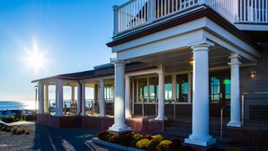 A two-story building with a balcony, large windows, and a covered outdoor area with steps leading to the entrance. - The Shore House (Narragansett)