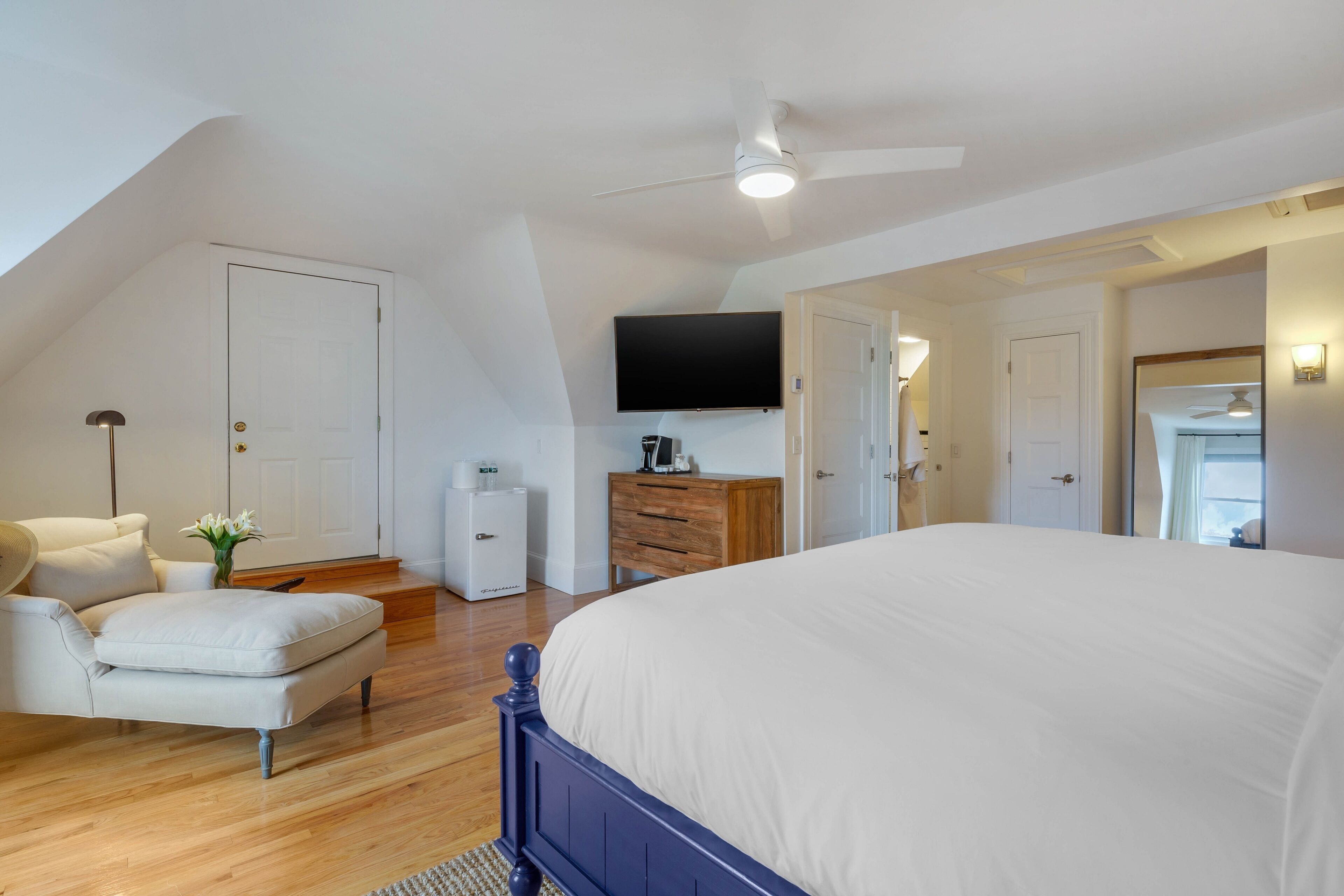 A bedroom with a large bed, a ceiling fan, a flat-screen TV, a dresser, and a chair.