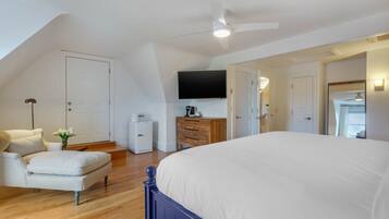 Een slaapkamer met een groot bed, een plafondventilator, een flatscreen televisie, een dressoir en een stoel.