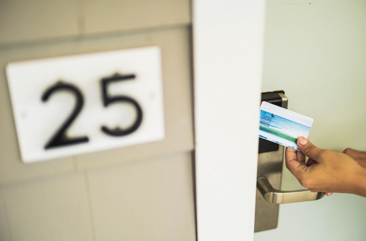 A hand holding a card near a door with a number sign indicating room 25.