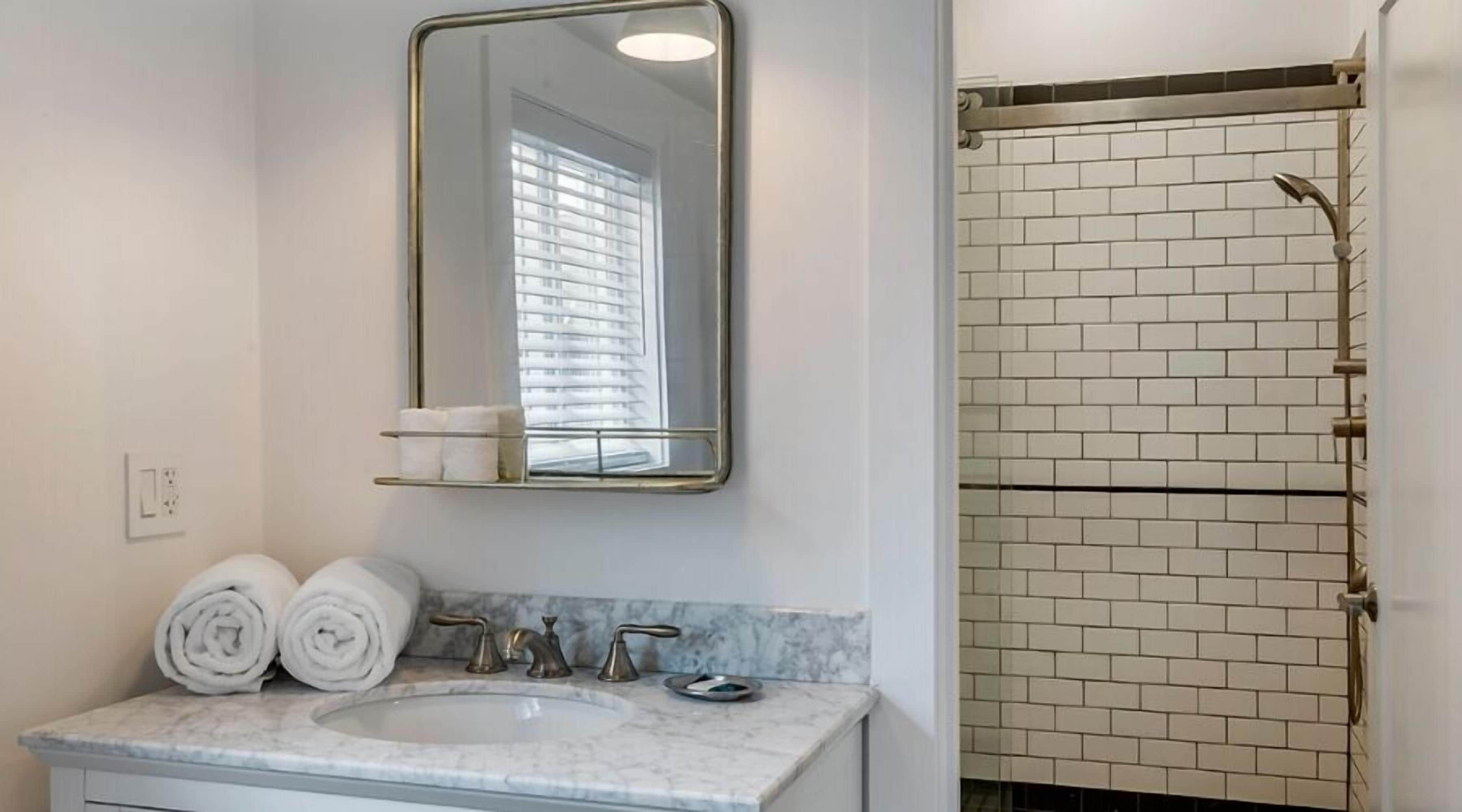 Un baño con lavamanos de mármol, dos toalleros, un espejo y una ducha con pared de azulejos.