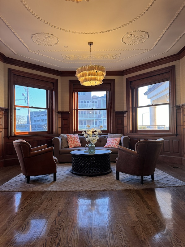 A room with a large window, a chandelier, a sofa, two armchairs, and a coffee table.