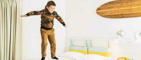A child jumping on a bed in a room with a wooden headboard, a bedside lamp, and a vintage telephone.