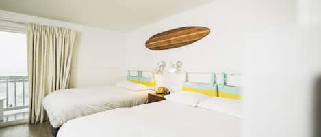 A hotel room with two beds, a wooden headboard, a nightstand with a lamp, and a window with curtains.