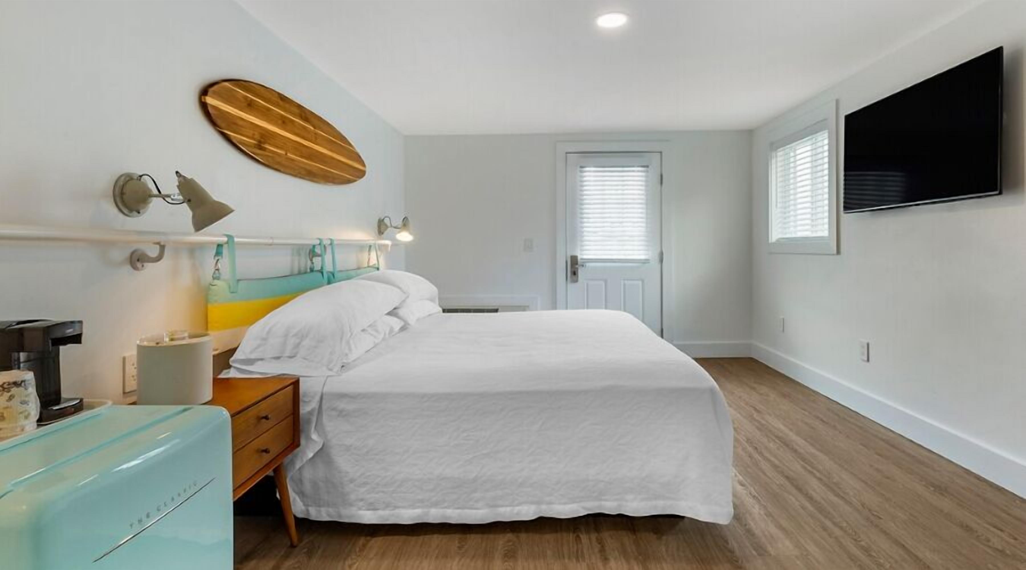 A bedroom with a bed, bedside table, lamp, and a television on the wall.