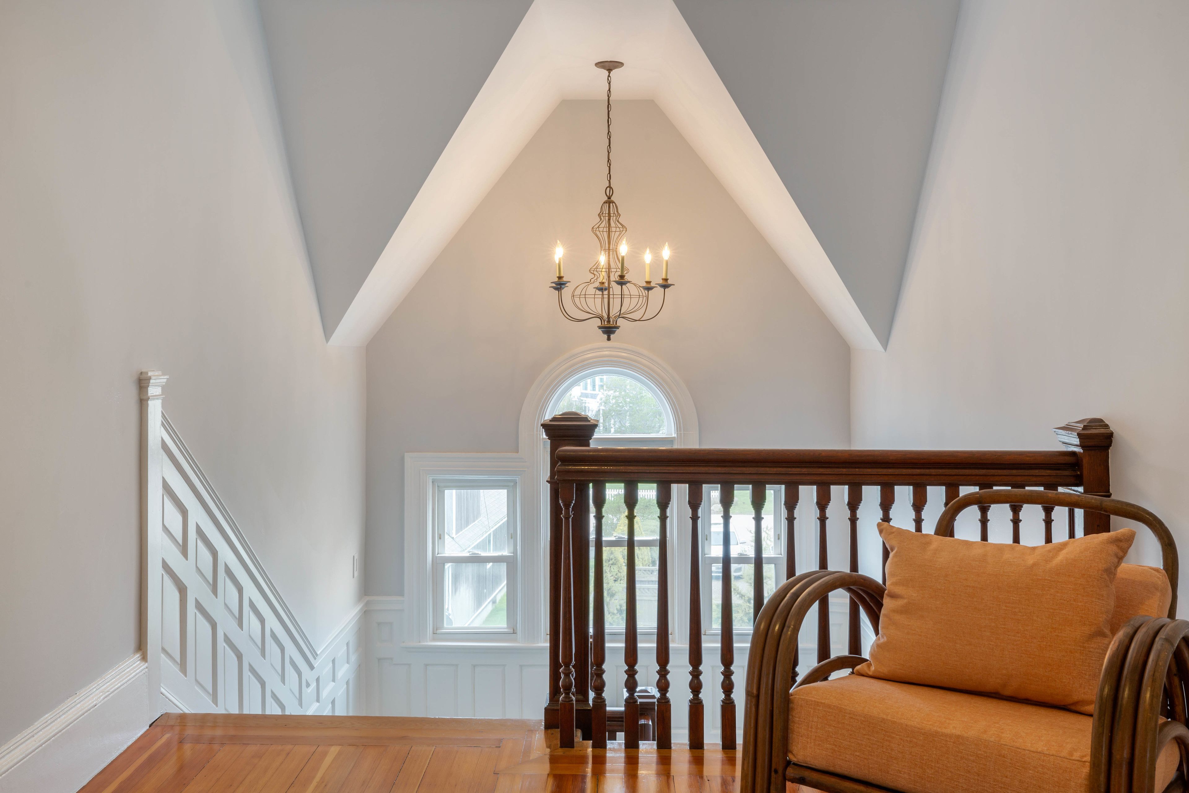 A room with a wooden staircase, a chandelier, and a window with a view.
