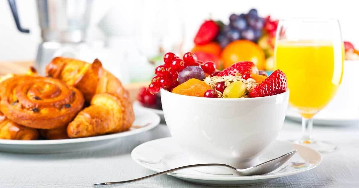 Un desayuno con una ensalada de frutas, un plato de pasteles y un vaso de jugo de naranja.