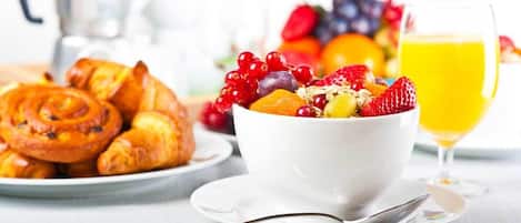 A breakfast setting with a bowl of fruit salad, a plate of pastries, and a glass of orange juice.