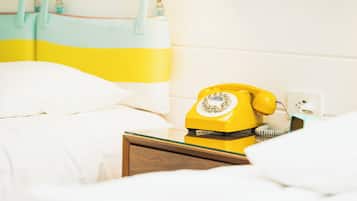 A bed with white bedding and a yellow rotary phone on a bedside table.
