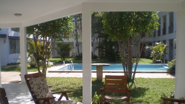 A covered outdoor seating area with wooden chairs and a table, overlooking a swimming pool and greenery. - Ruta del Sol (San Bernardino)