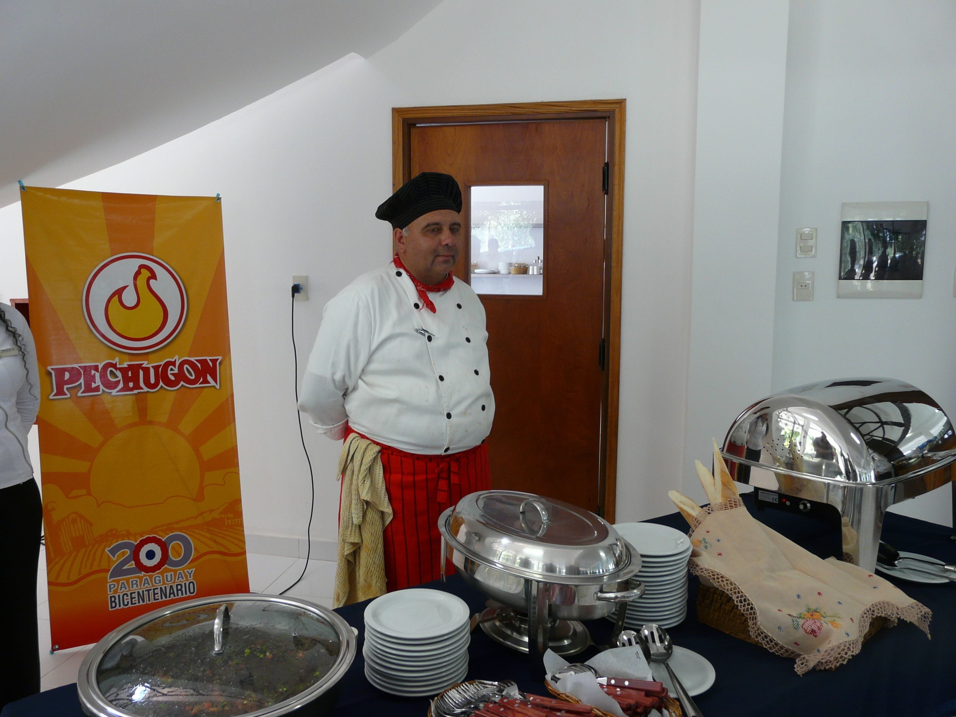 Montaje de bufé con diversos platos y utensilios, un chef con uniforme y un cartel que indica una celebración por 200 años.