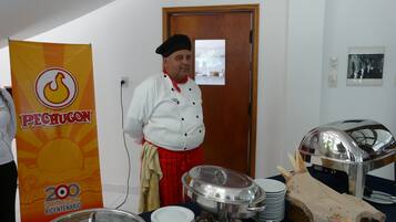 Montaje de bufé con diversos platos y utensilios, un chef con uniforme y un cartel que indica una celebración por 200 años.