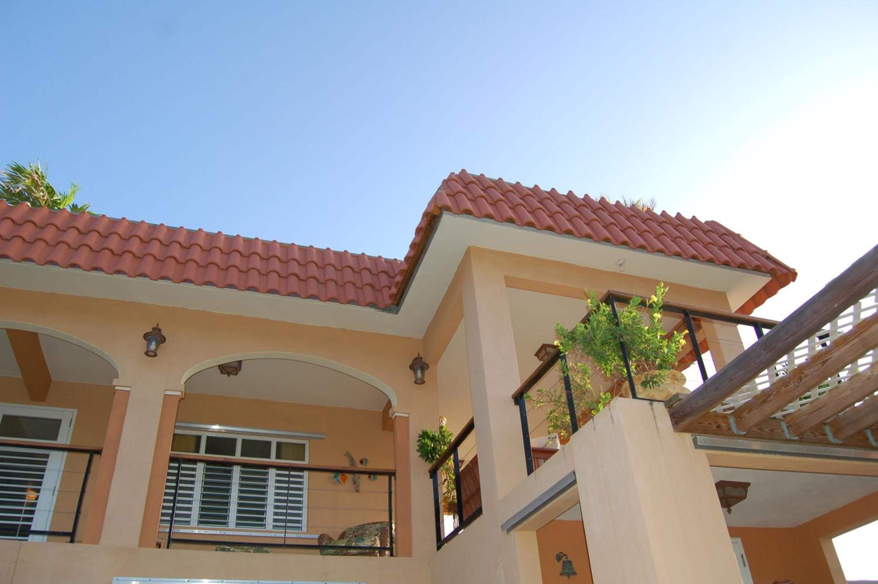 A building with a red-tiled roof, multiple balconies with railings, and a clear sky.