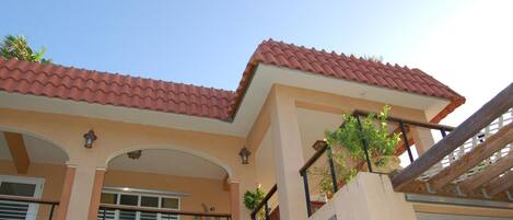 A building with a red-tiled roof, multiple balconies with railings, and a clear sky.