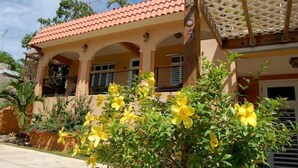 A two-story house with a red-tiled roof, a covered porch, and yellow flowering plants in the foreground.