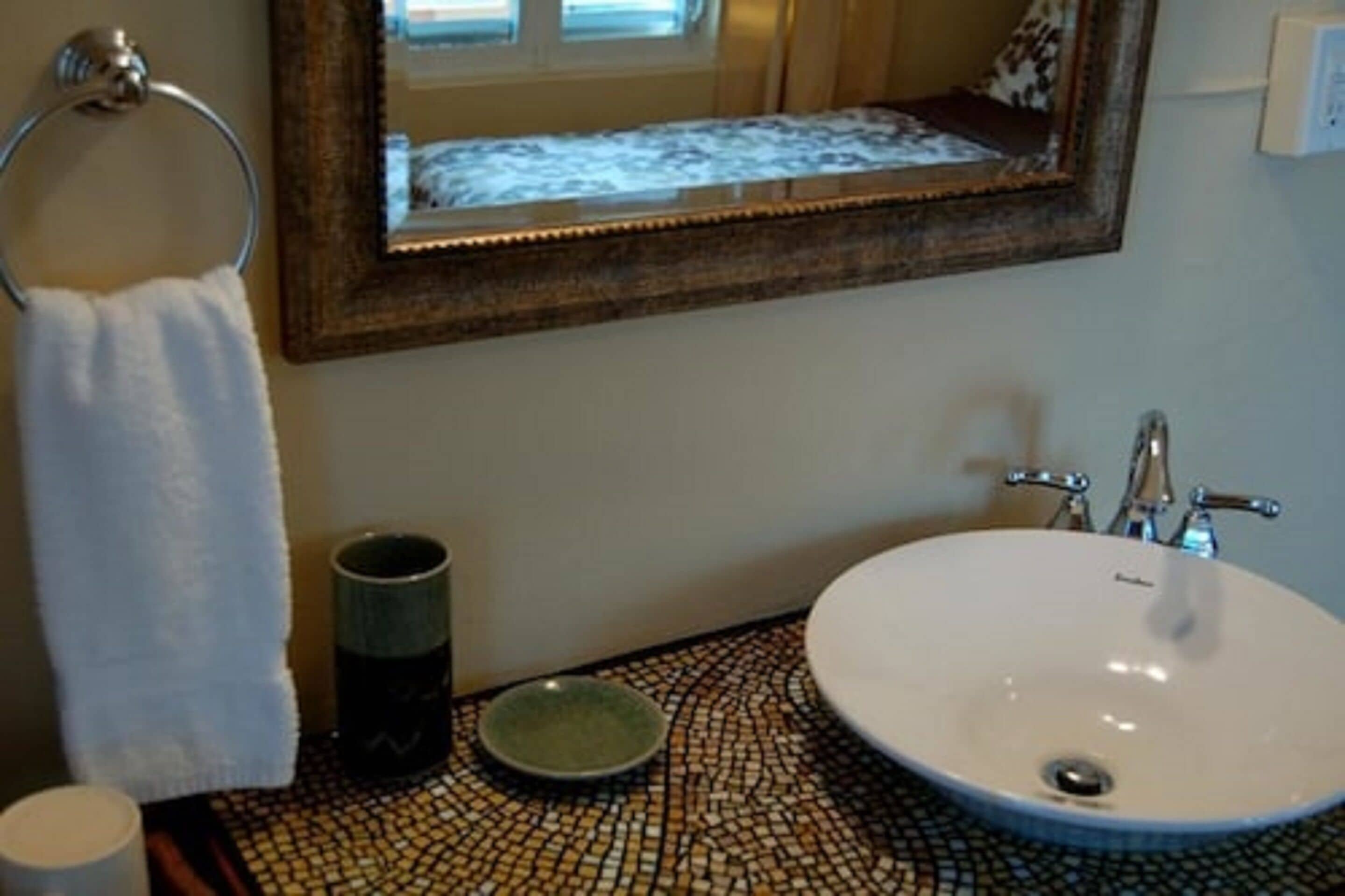 A bathroom with a round sink, a mirror, a towel ring, and a mosaic-patterned countertop.
