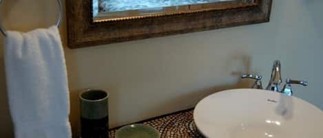 A bathroom with a round sink, a mirror, a towel ring, and a mosaic-patterned countertop.