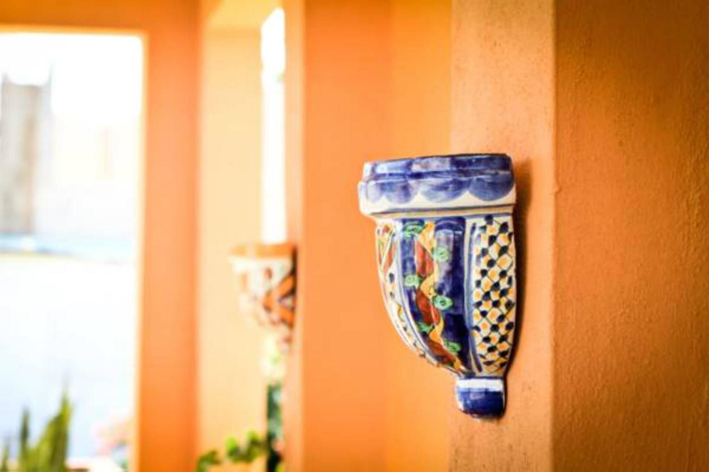 A decorative ceramic wall piece with a blue and yellow pattern, mounted on a wall with a warm orange hue.