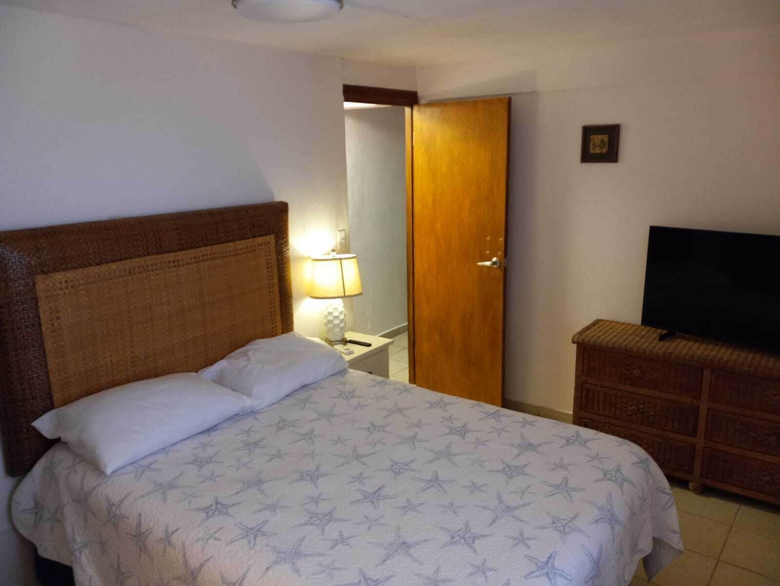 Une chambre d’hôtel équipée d’un lit, d’une télévision, d’une armoire en bois et d’une porte donnant accès à une salle de bain.
