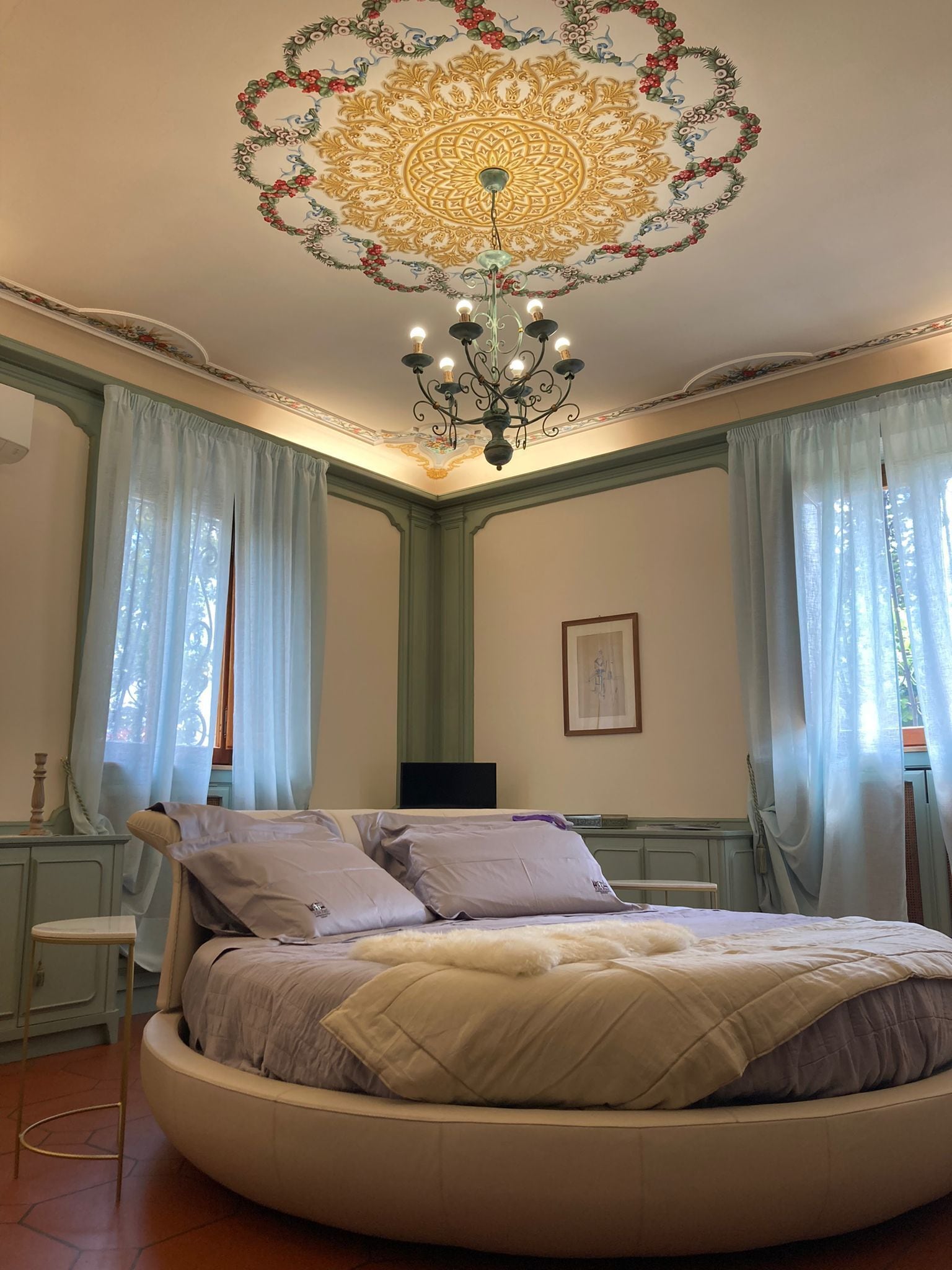 Un lit rond dans une pièce dotée d’un plafond décoratif, de rideaux légers et d’un lustre.