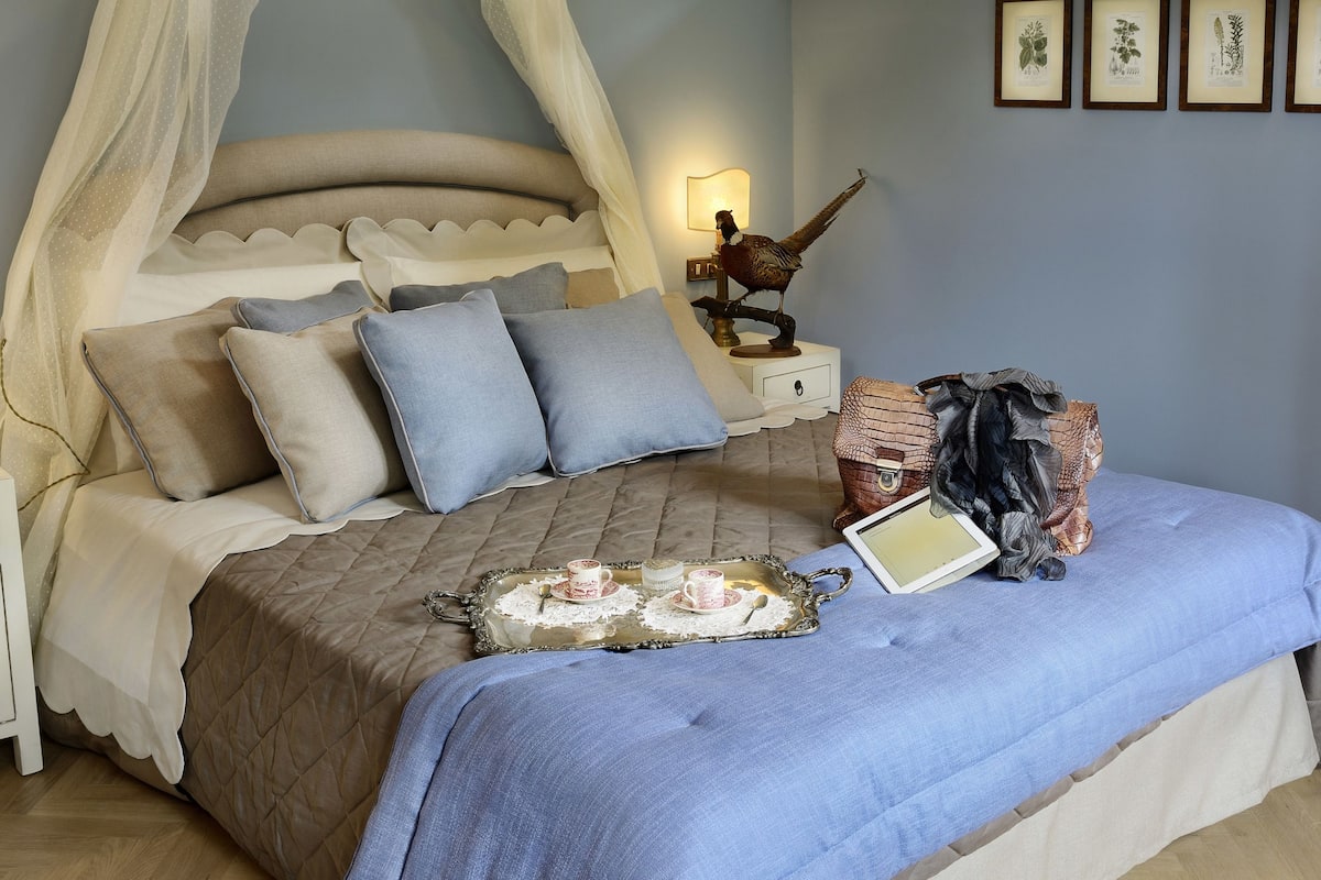 A bedroom with a canopy bed, bedside table with a lamp, and framed pictures on the wall.