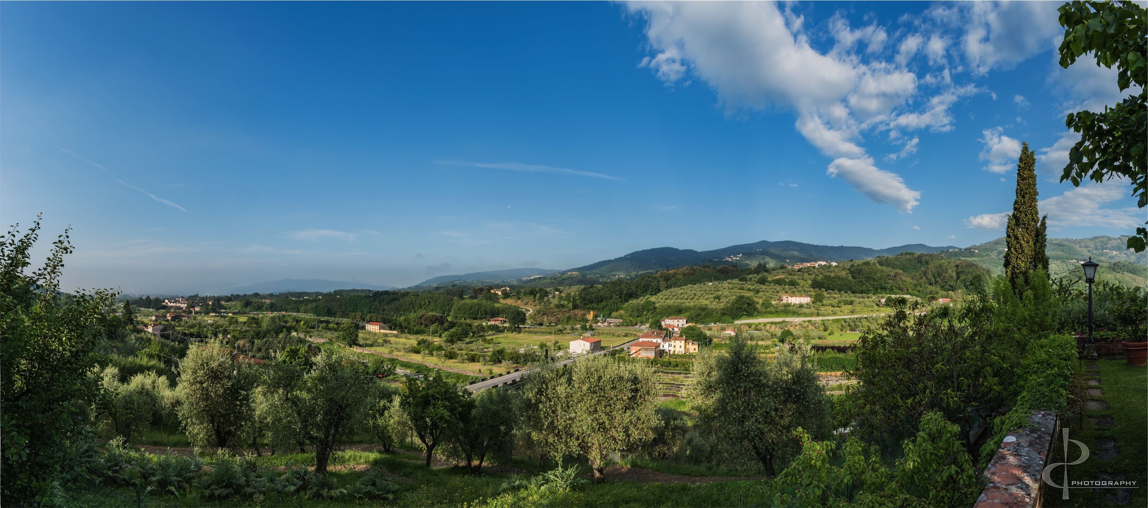 A rural landscape with rolling hills, scattered buildings, and a clear sky.