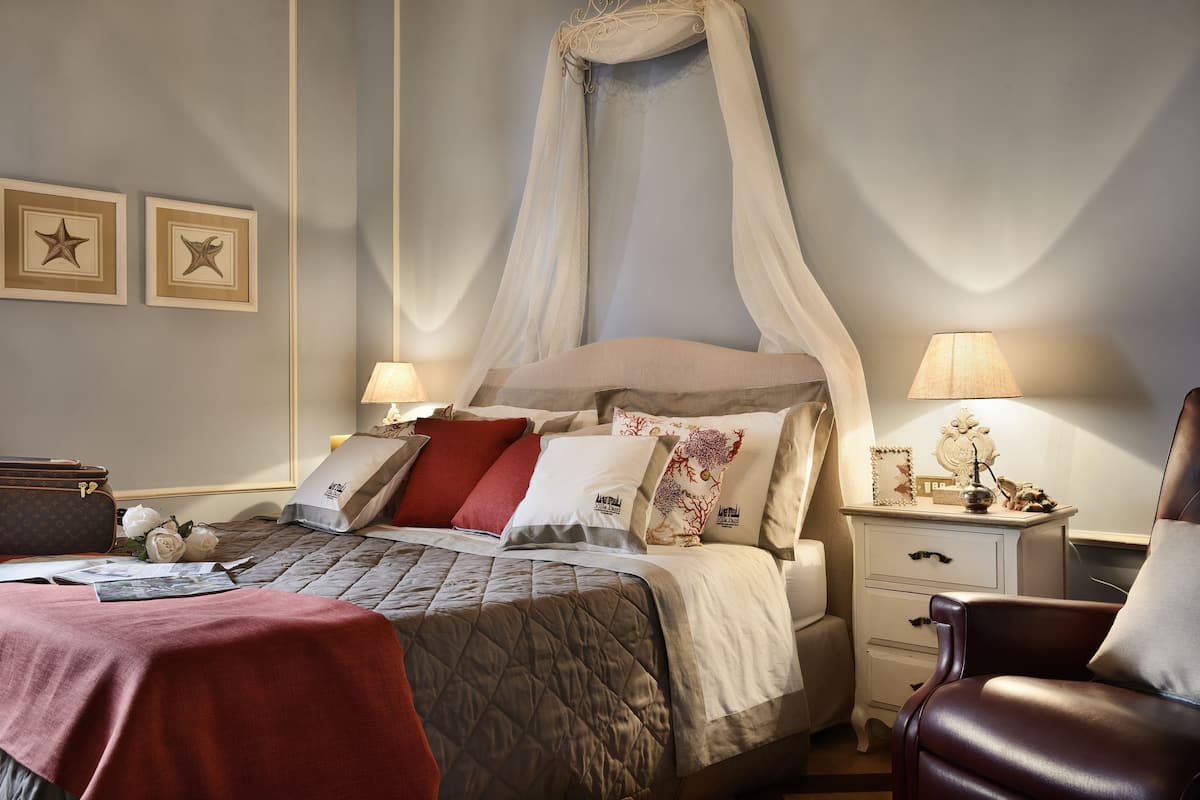 A neatly arranged bedroom with a four-poster bed, bedside tables, a chair, and framed pictures on the wall.