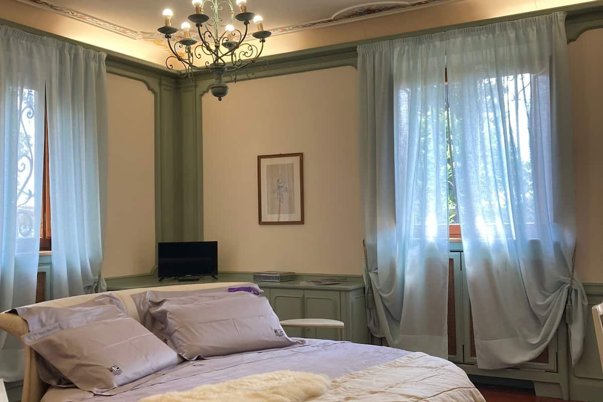 A circular bed with a fluffy white blanket, a chandelier, and light curtains on windows.