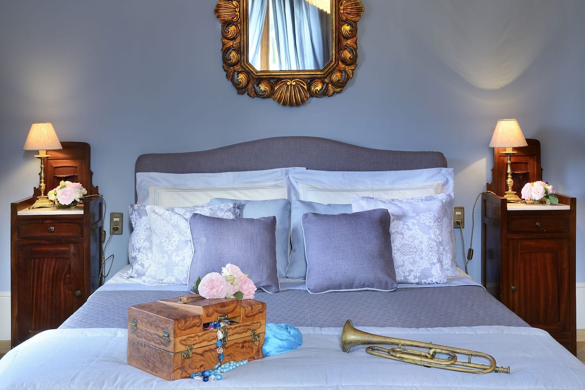 A neatly made bed with a quilted bedspread, a wooden chest of drawers, and a brass trumpet on the bed.
