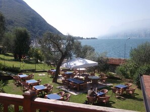 An outdoor seating area with tables and chairs, overlooking a body of water and mountains. - Albergo Navene (Malcesine)