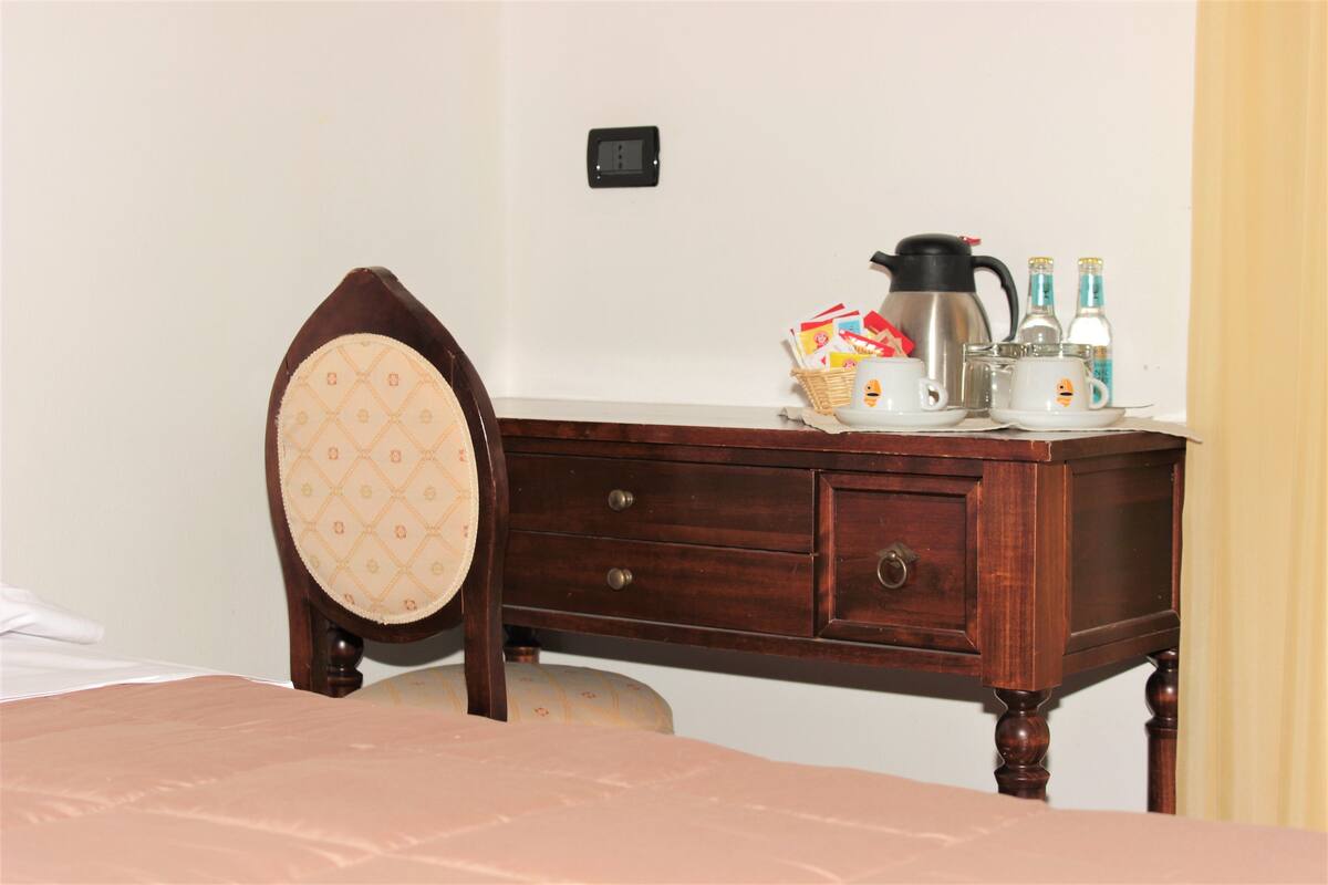 Un aparador de madera con cajones, una silla con cojín estampado y una cafetera encima.