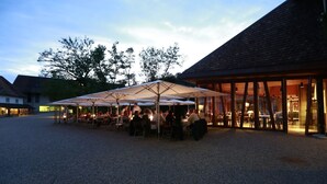 An outdoor dining area with tables and umbrellas, surrounded by buildings with a gravel ground. - Stiftung Kartause Ittingen (Warth-Weiningen)