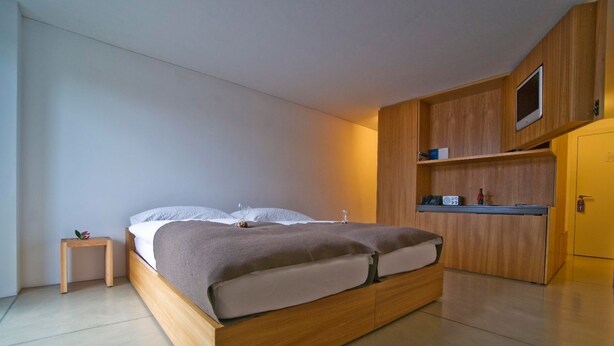 Ein modernes Schlafzimmer mit einem hölzernen Bett, einem kleinen Nachttisch und integrierten Holzregalen mit einem Fernseher.