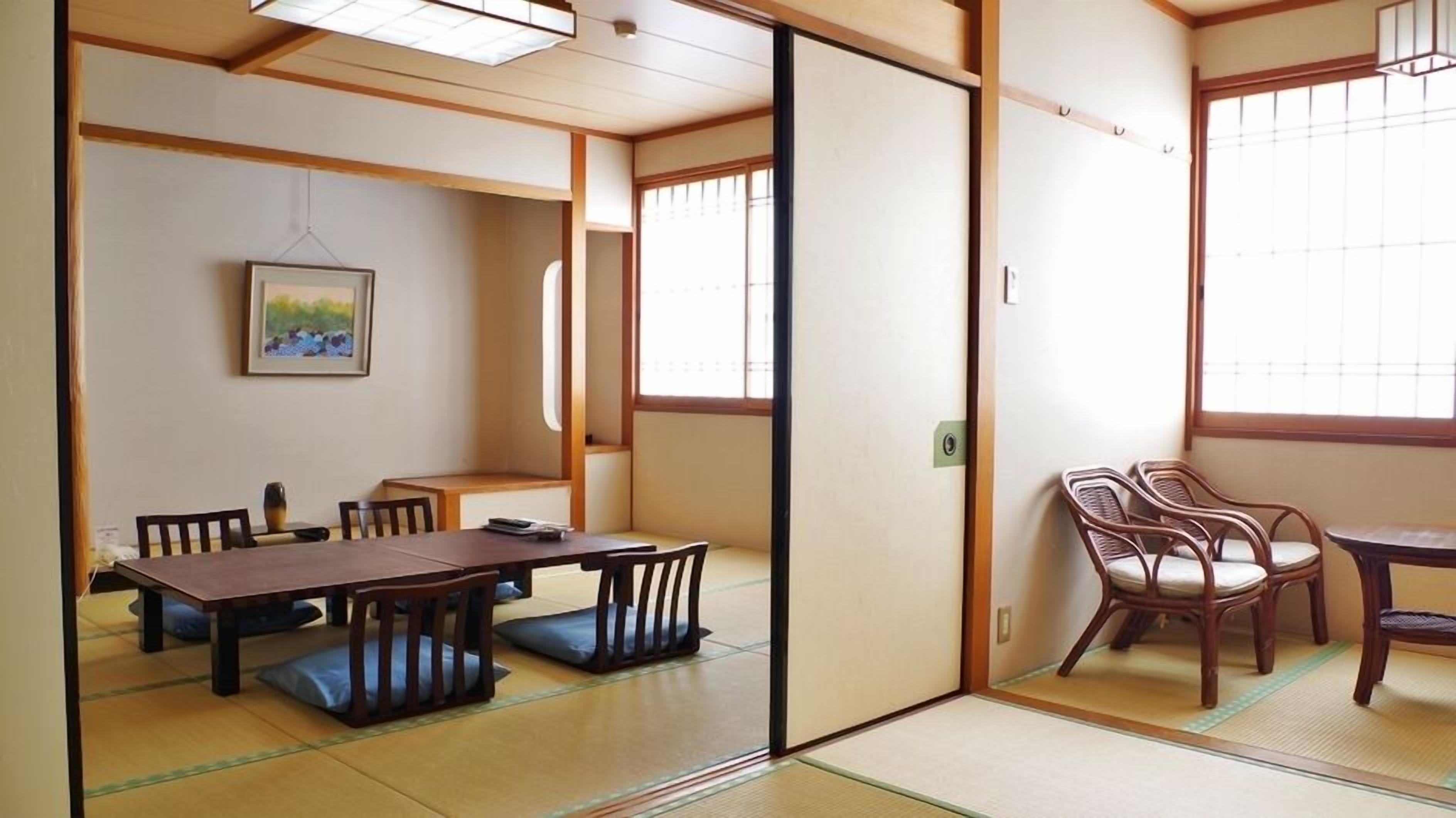 A traditional Japanese room with tatami flooring, a low table with chairs, a sliding door, and a window with shoji screens.