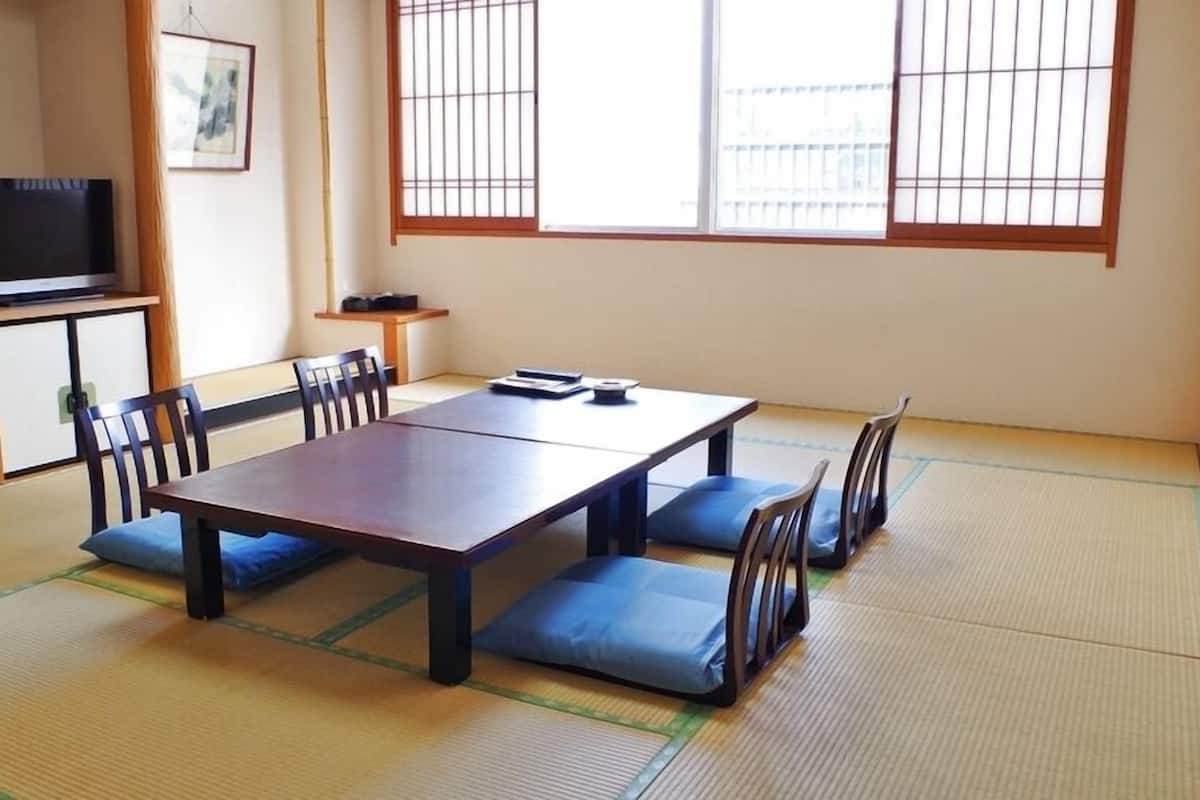 Una habitación con tatami, una mesa baja, sillas, un televisor y un cuadro en la pared.