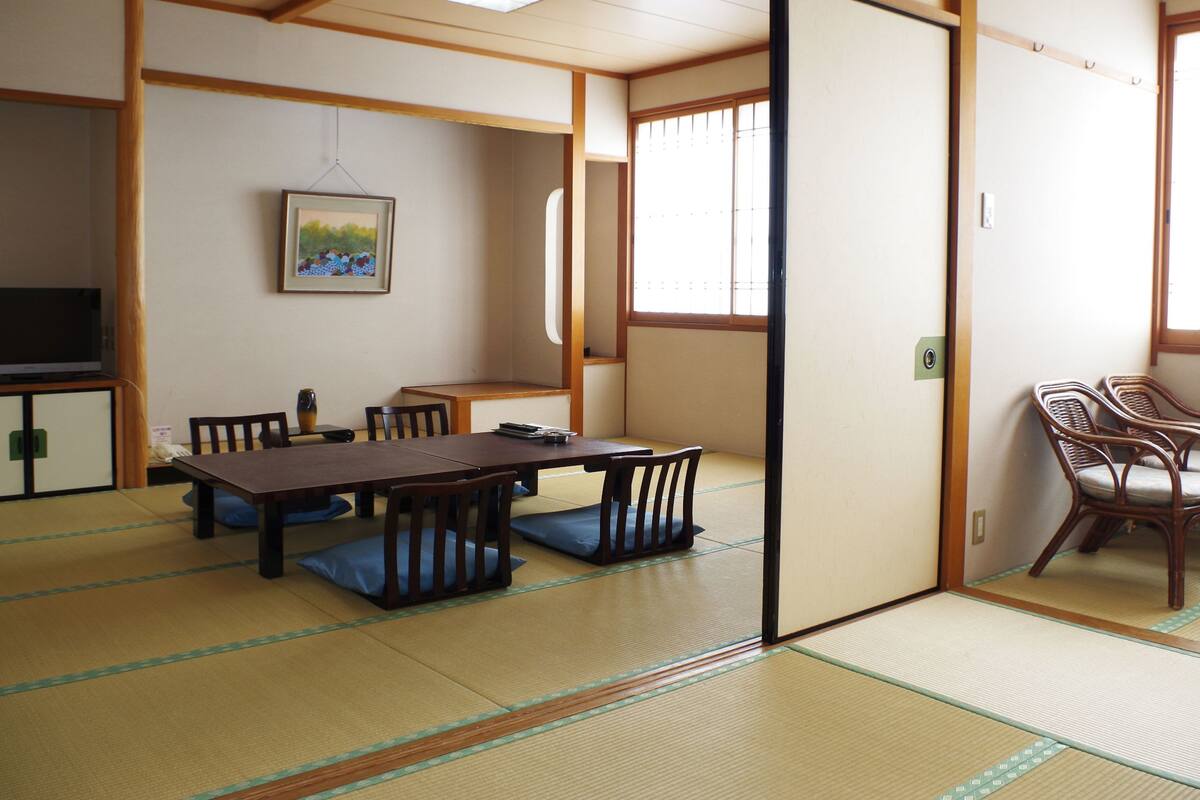 Una habitación japonesa tradicional con suelo de tatami, una mesa baja con cojines y una puerta corredera.