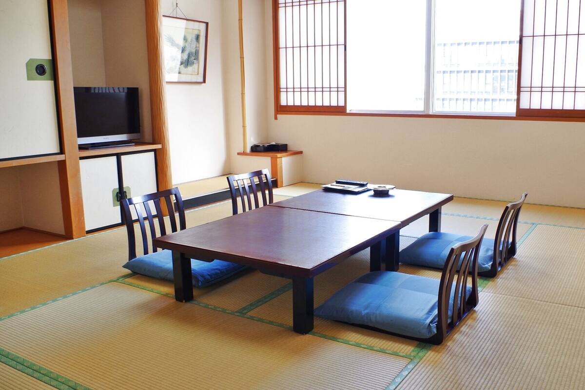 Una habitación con esteras de tatami, una mesa baja y sillas, un televisor y un cuadro en la pared.