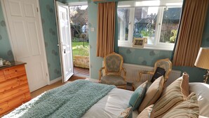 A bedroom with a bed, a wooden dresser, a chair, and a window with a view of the garden. - Fairlight Lodge (King's Lynn)