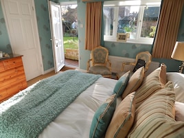 Quarto com cama, penteadeira de madeira, cadeira e janela com vista para o jardim.